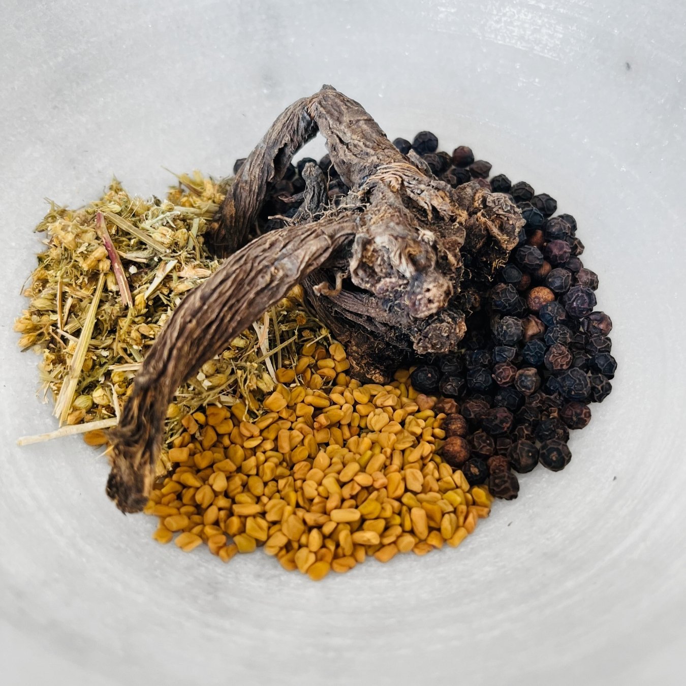 A variety of dried herbs and spices arranged on a surface, including what appears to be fenugreek seeds, black peppercorns, yarrow, and valerian root, consistent with the ingredients listed for the Rage Reducer Tea Bags product.