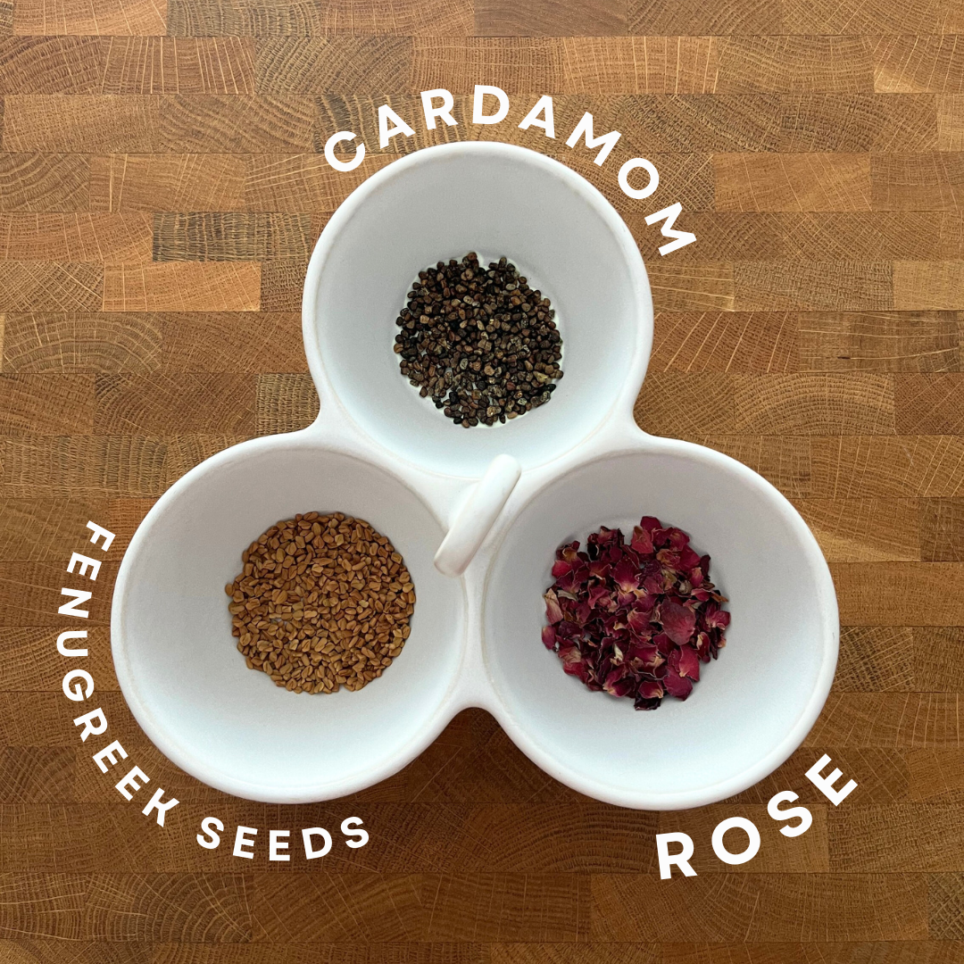 Three white bowls with cardamom, fenugreek seeds, and rose on a wooden surface.