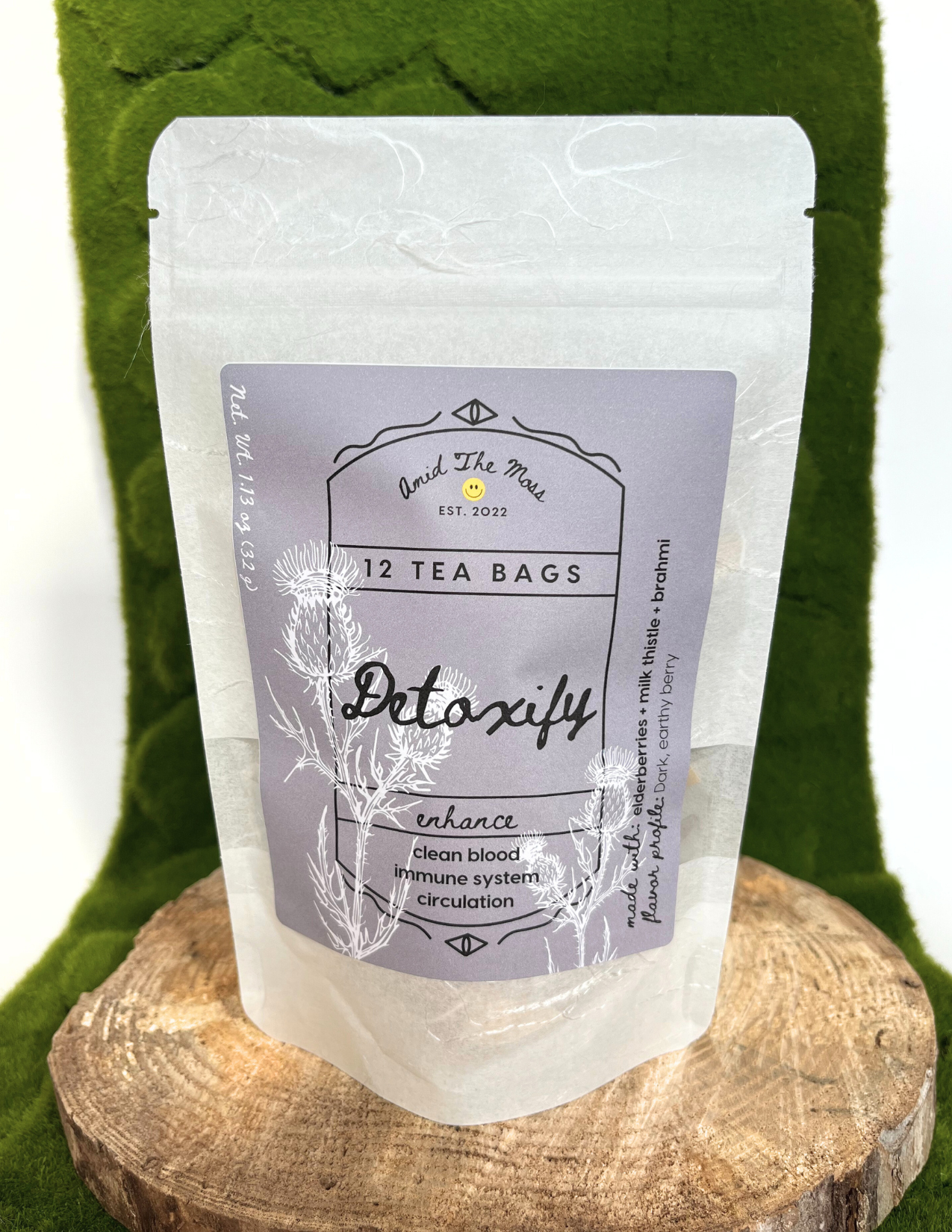 Tea bag package labeled 'Detoxify' on a wooden stand with a green fabric background