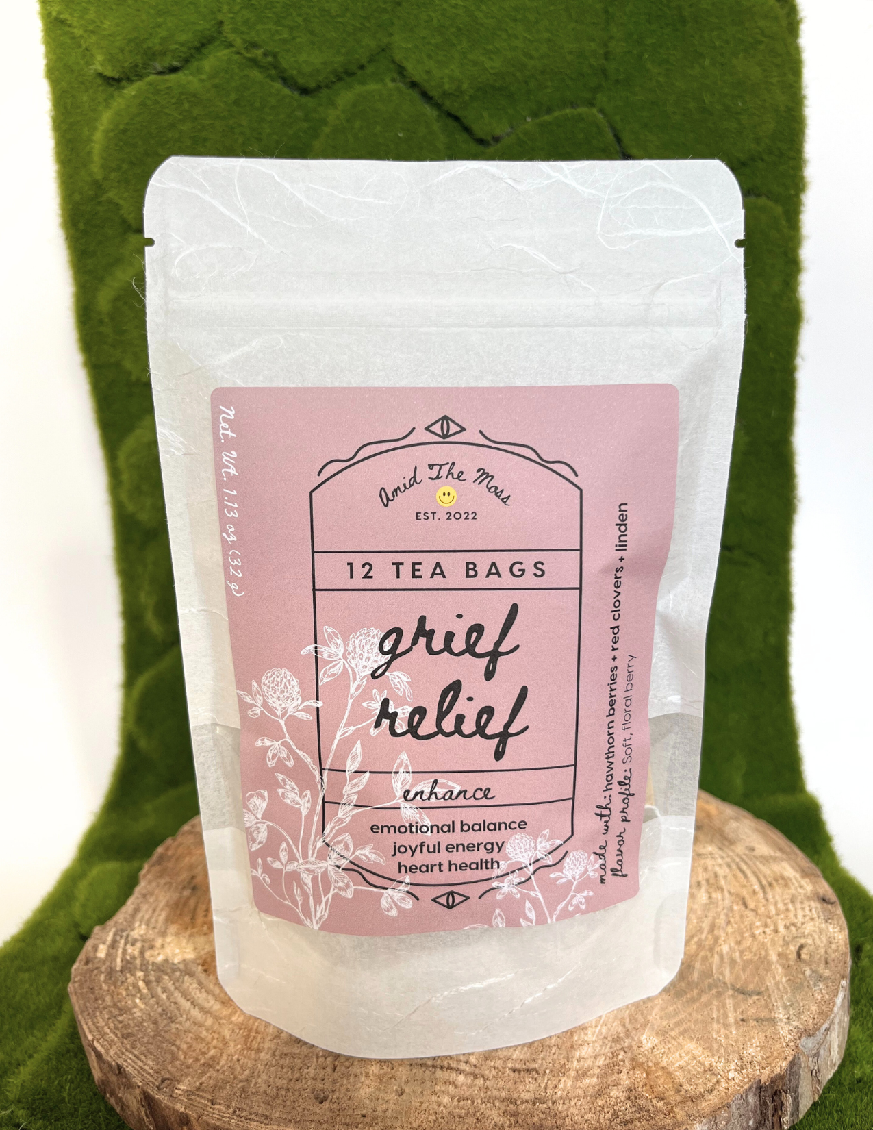 Tea bag package labeled 'Grief Relief' on a wooden block with green fabric background